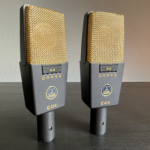 Zwei Mikrofone auf einem Holzuntergrund. Die Mikrofone stehen nebeneinander und haben einen goldenen Mikrofonkorb, unter diesem ist ein Umschalter sowie das goldene AKG Logo zu sehen. Stereopärchen AKG C 414 XL II Studio Klassiker