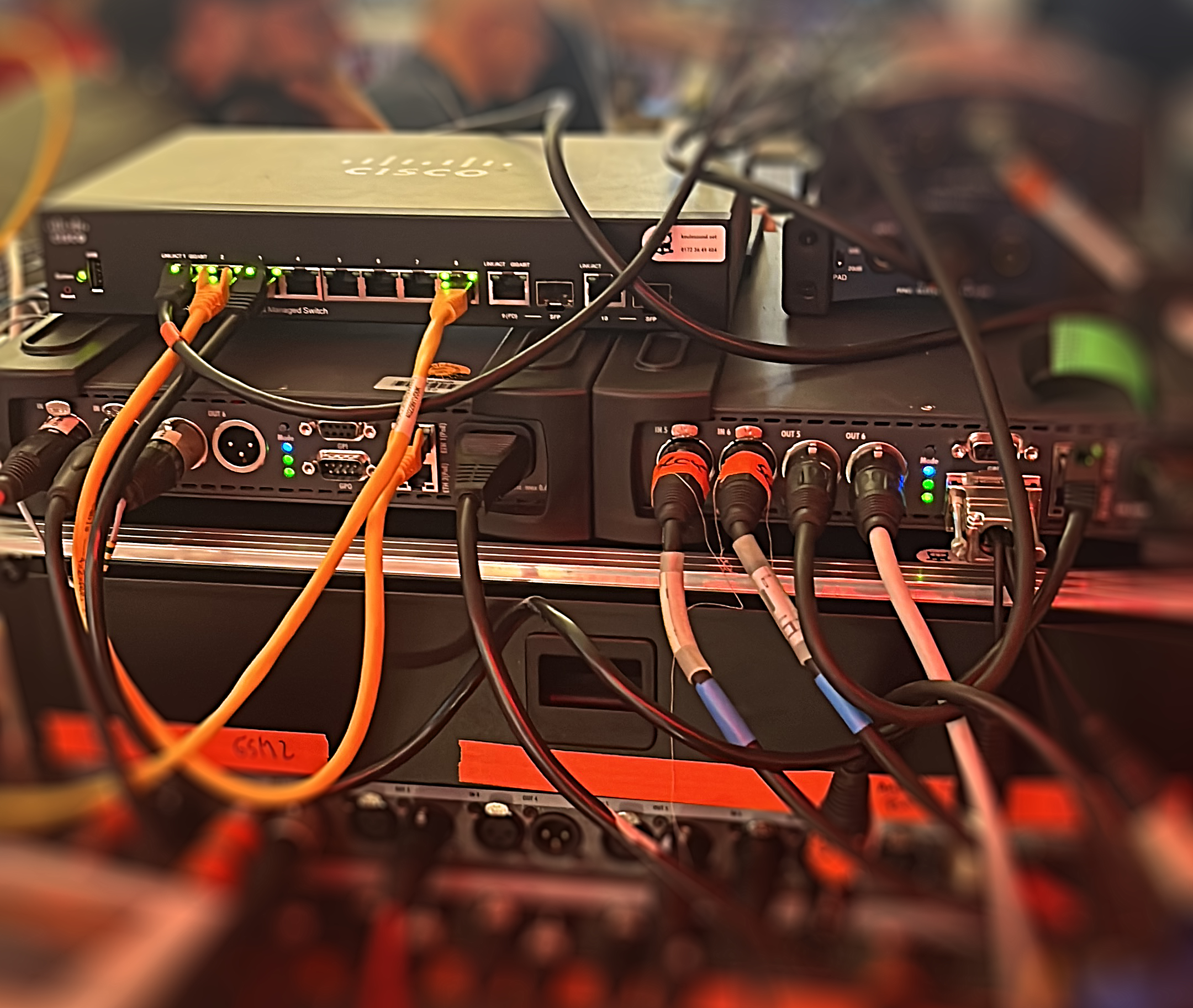Studiogeräte, oben ein Switch für Netzwerk viele Kabel gehen zu unterschiedlichen Geräten, Unter dem Switch zwei Geräte die mit Audiokabel angeschlossen sind. Riedel Bolero und Riedel Artist