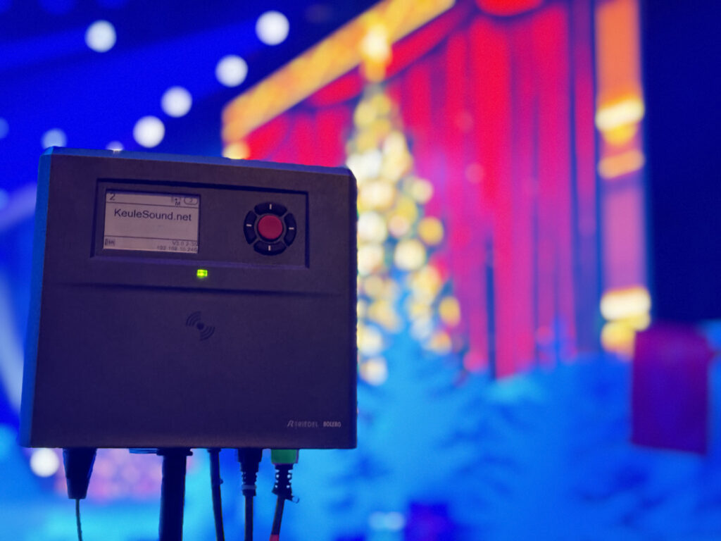 Eine viereckige Bolero DECT Antenne, vor einer Bühne. Auf dieser steht ein Leuchtender Weihnachtsbaum vor einem toten Samtvorhang.